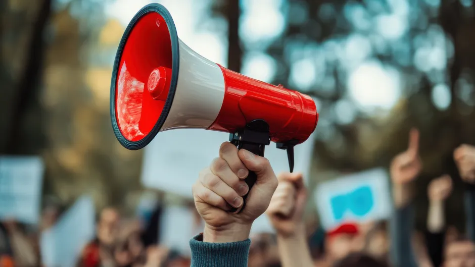 Megaphon im Großformat, im hintergrund (unscharf) eine Demonstration